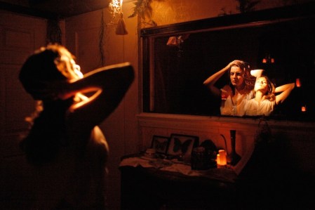 A image of a lady standing infront of the mirror seeing it reflecting two of her own. This is a scene from the immersive show called then she fell.